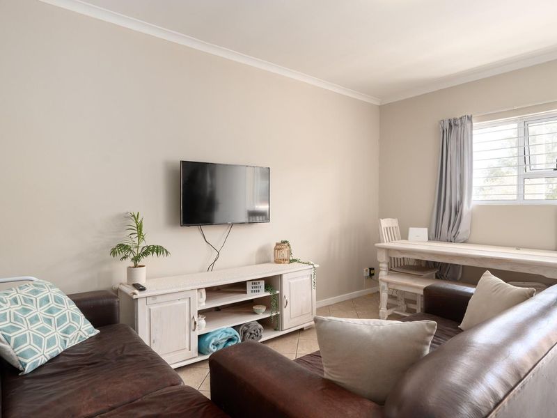 A comfortable living room featuring tiled flooring, neutral wall tones, and a window with security bars, providing a functional and well-lit living space.