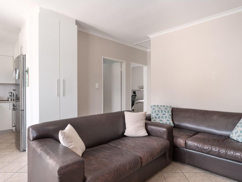 Open plan living area featuring tiled flooring and a compact kitchen with built-in cabinetry, seamlessly connecting to the rest of the apartment.