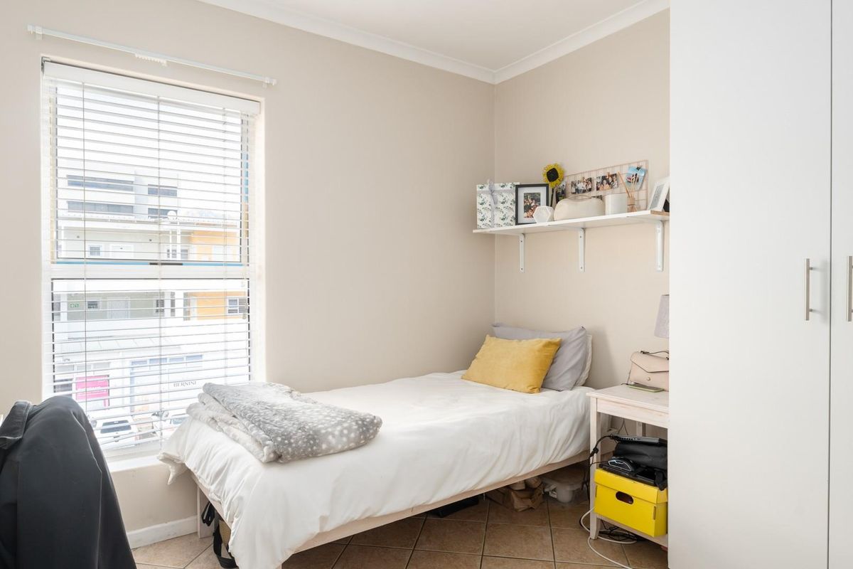 A bright bedroom featuring tiled flooring, a built-in wardrobe, and a window fitted with venetian blinds.