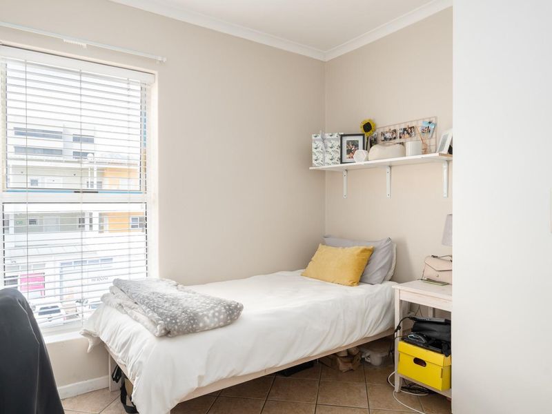 A bright bedroom featuring tiled flooring, a built-in wardrobe, and a window fitted with venetian blinds.