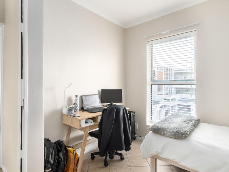 A well-lit bedroom featuring tiled flooring, built-in wardrobe storage, and venetian blinds, offering a functional and neutral living space.