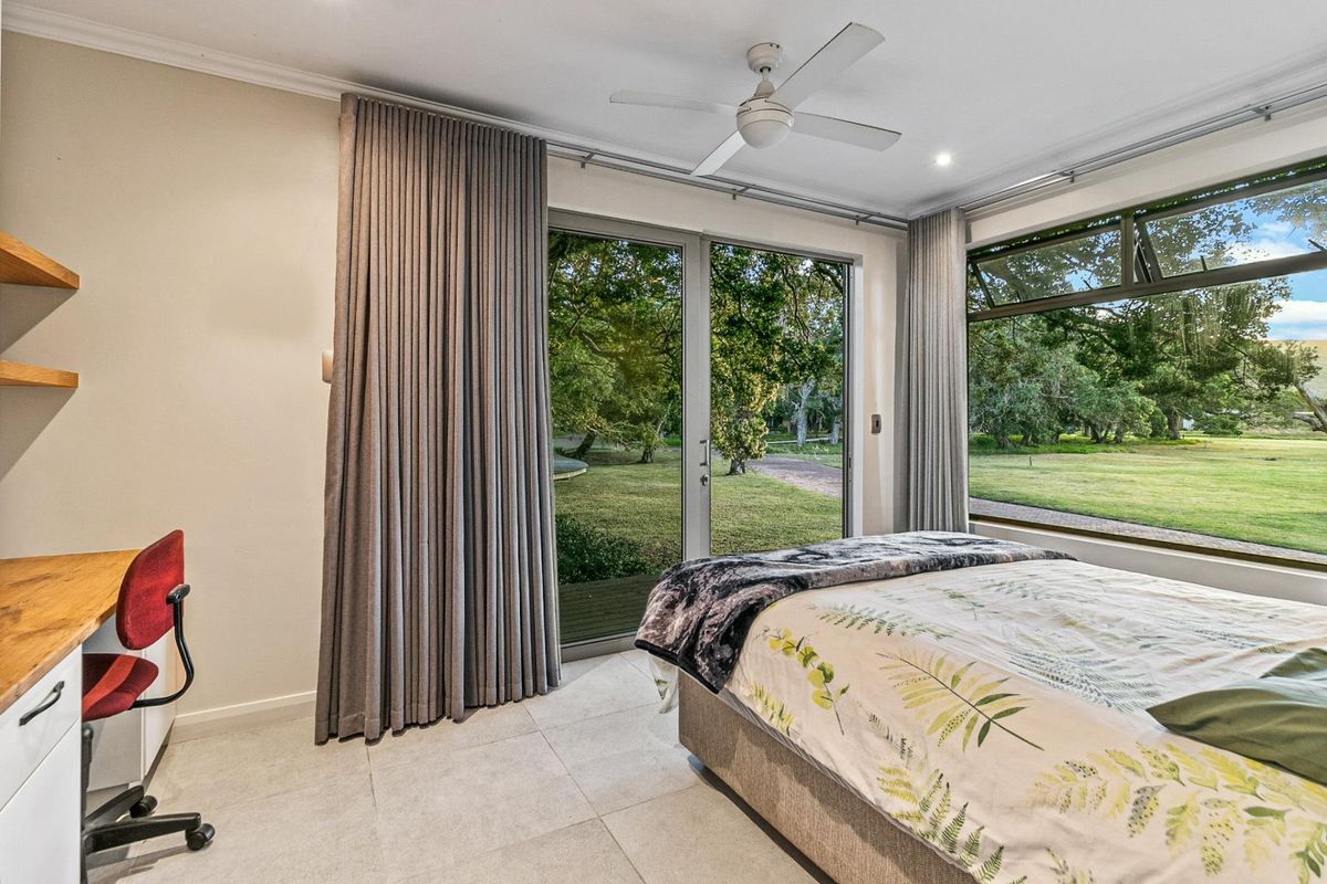 A bright bedroom featuring large glass sliding doors, floor-to-ceiling curtains, a ceiling fan, and tiled flooring with views of the surrounding garden.