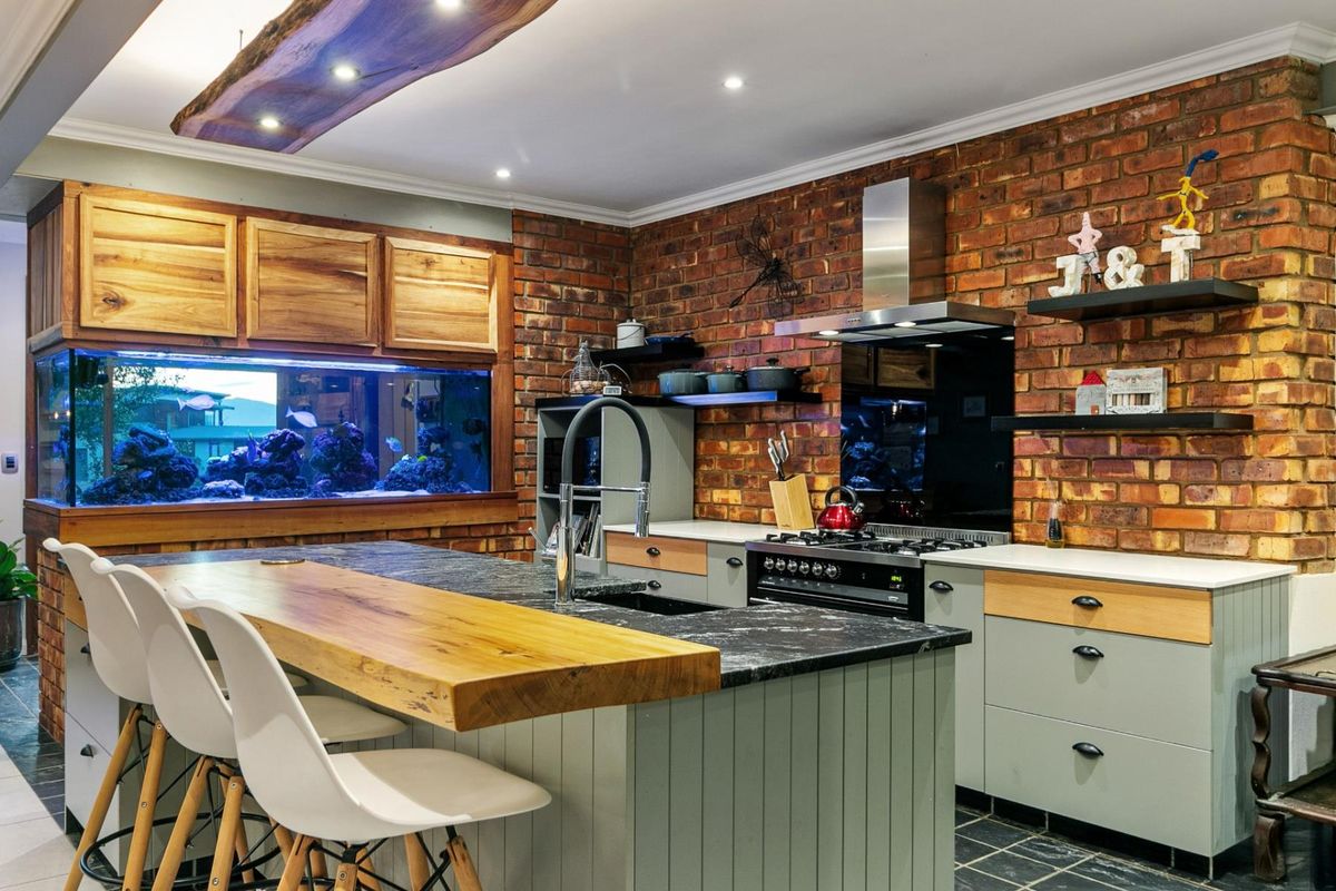 A rustic-style kitchen featuring exposed brick walls, a large built-in aquarium, a central island with a live-edge wood breakfast bar, and modern cabinetry.