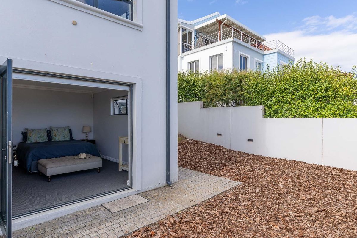 A ground floor bedroom with large bi-fold doors opening onto a paved patio area and a landscaped rear garden with retaining walls.