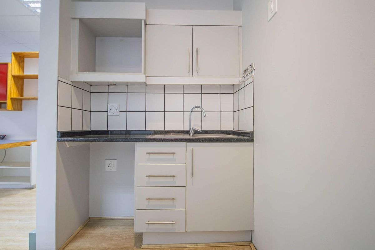 Compact office kitchenette featuring built-in cabinetry, a dark stone countertop, a stainless steel sink, and tiled backsplash.
