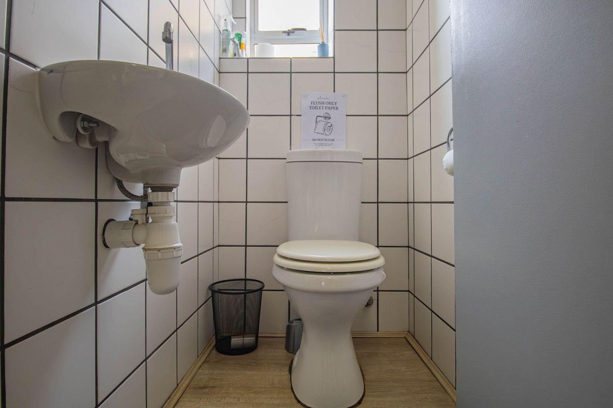 A compact office restroom featuring white wall tiles, a wall-mounted basin, and a standard toilet.