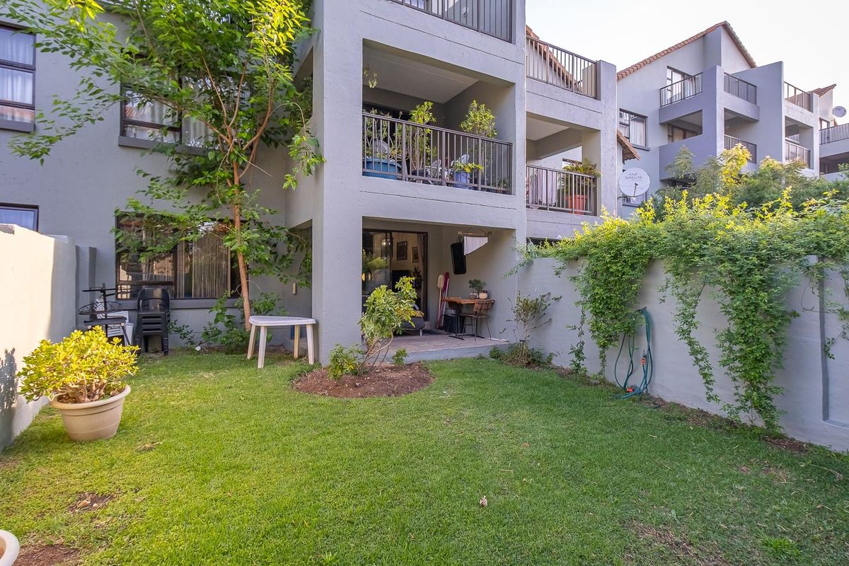 A private ground-floor garden area featuring a covered patio, lawn, and boundary wall, providing direct access to the apartment through sliding glass doors.