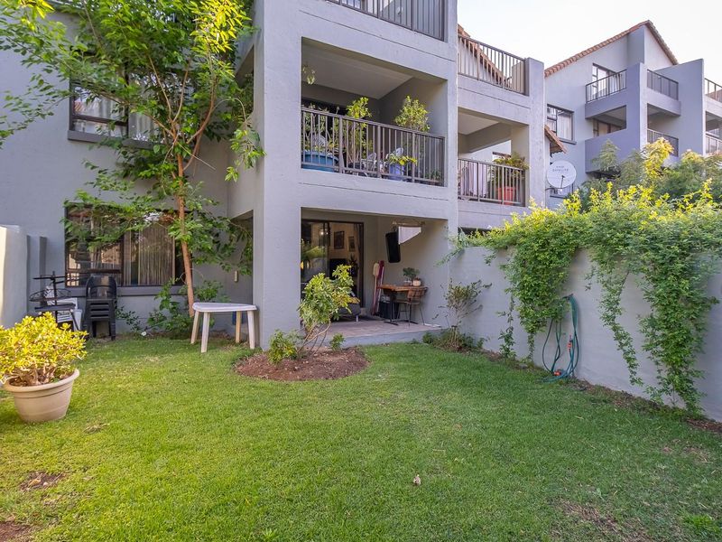 A private ground-floor garden area featuring a covered patio, lawn, and boundary wall, providing direct access to the apartment through sliding glass doors.