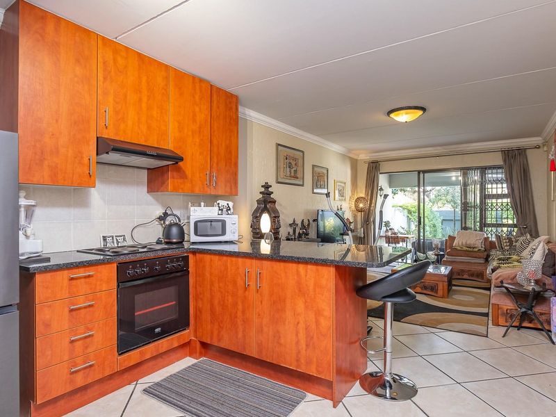 Open-plan kitchen and living area featuring wood-finish cabinetry, granite countertops, built-in appliances, and tiled flooring leading to a patio.