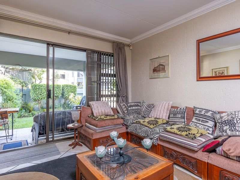 A living room featuring tiled flooring, crown molding, and a large sliding glass door providing direct access to a private patio and garden area.