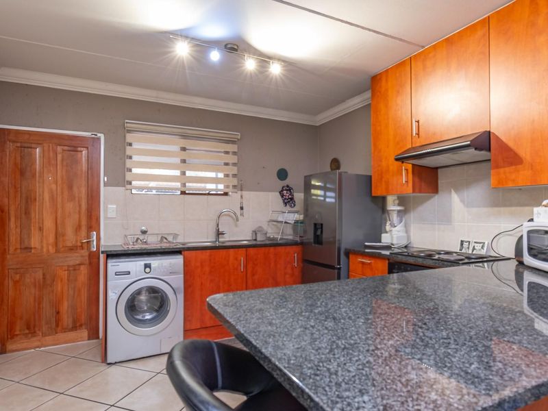 Functional kitchen featuring granite countertops, wooden cabinetry, built-in hob with extractor fan, and tiled flooring with space for a washing machine.