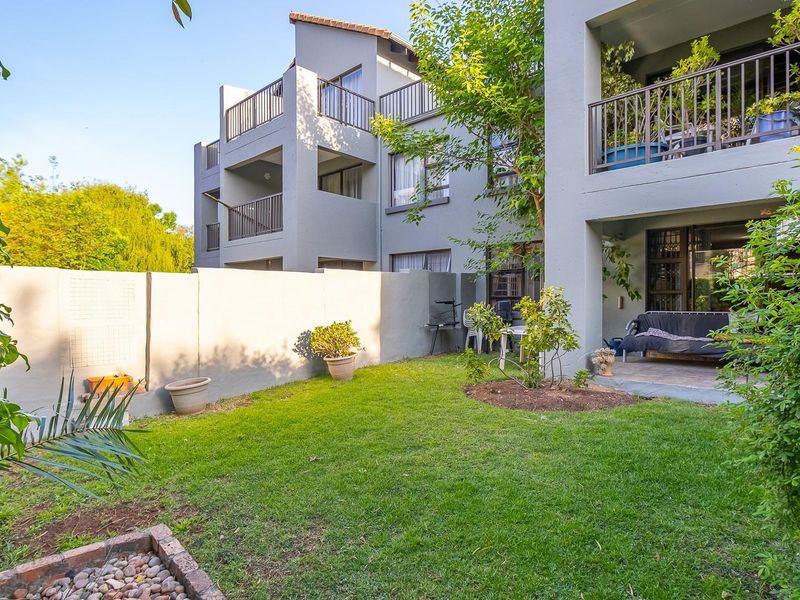 A private rear garden featuring a well-maintained lawn, a covered patio area, and boundary walls, attached to a multi-story apartment building.