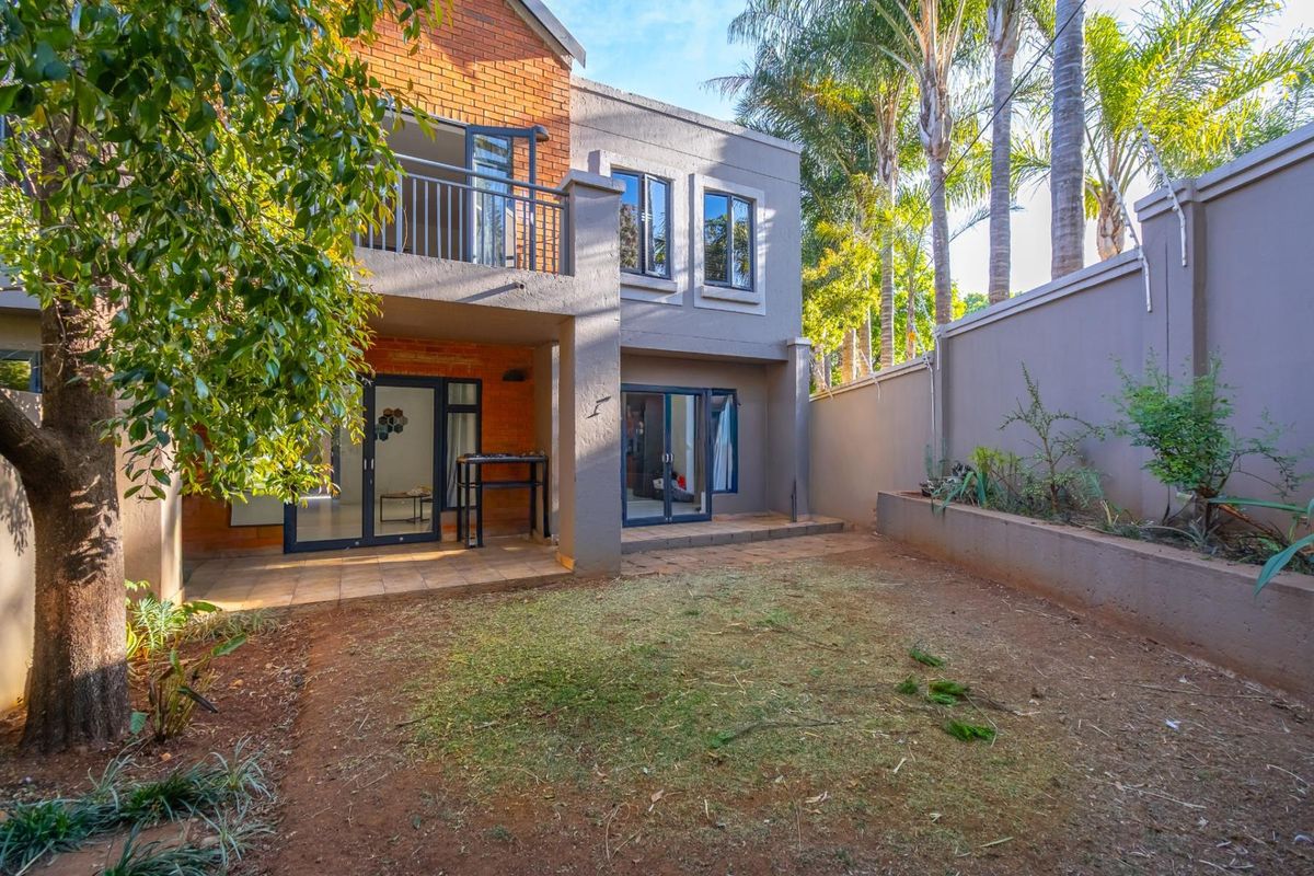 Rear view of the townhouse featuring a paved patio area, a small private garden, and a balcony accessible from the upper level.