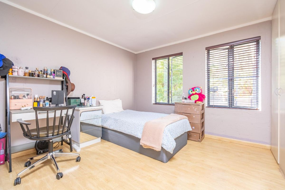 A functional bedroom featuring light wood-look flooring, dual windows with fitted blinds, and built-in wardrobe storage.