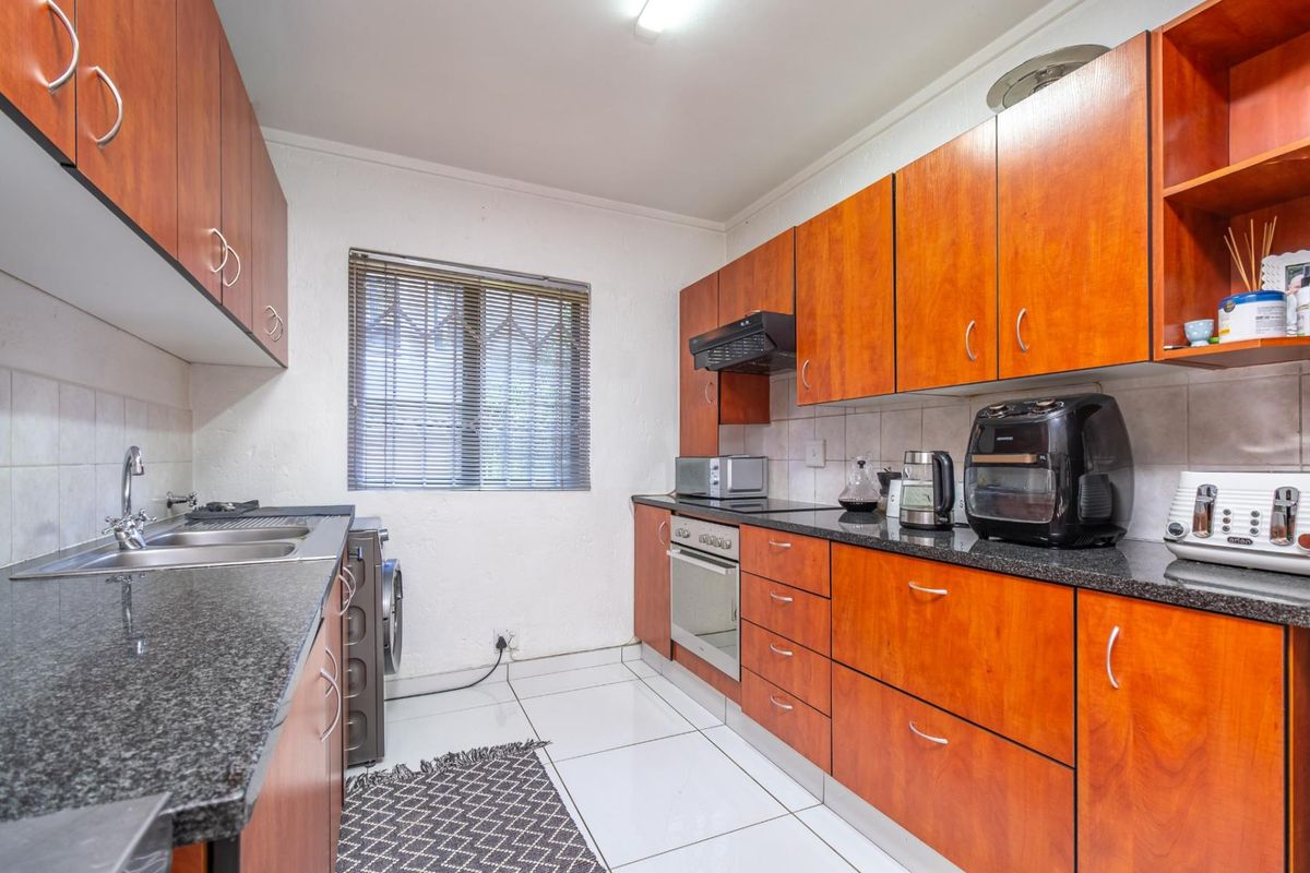 A functional kitchen featuring wood-finish cabinetry, granite countertops, a built-in oven, extractor fan, and a stainless steel sink with tiled flooring.