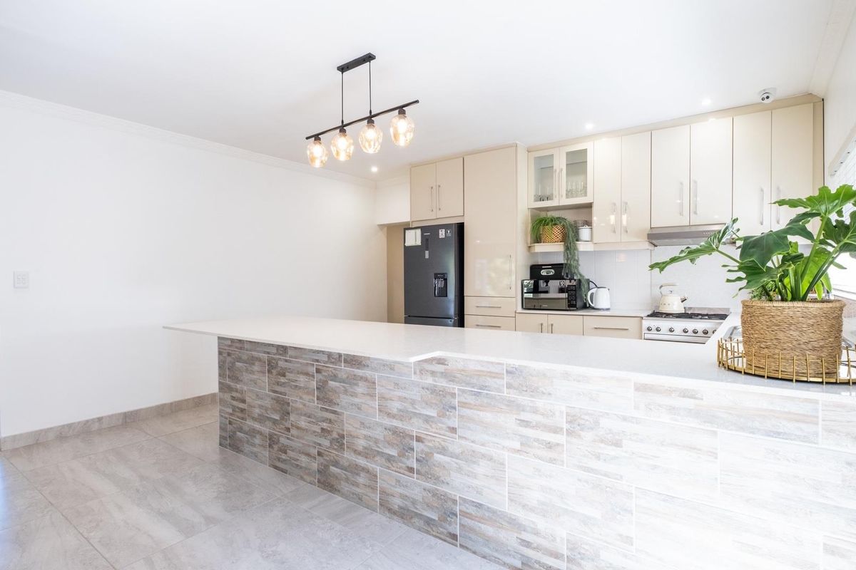 Modern kitchen featuring a stone-topped breakfast bar with tiled facade, sleek cabinetry, built-in stove, and contemporary pendant lighting.
