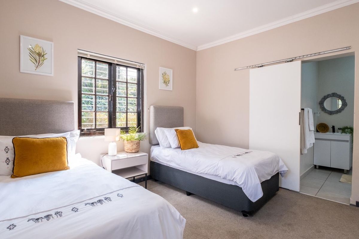 A well-maintained bedroom featuring neutral walls, carpeted flooring, a window with security bars, and an en-suite bathroom accessed via a sliding door.