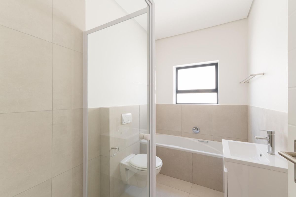 Modern bathroom featuring a glass-enclosed shower, a built-in bathtub, a wall-mounted toilet, and a sleek vanity basin with contemporary fixtures.