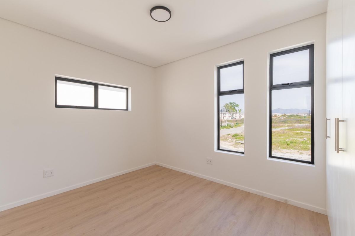 A bright, empty bedroom featuring modern light wood-look flooring, neutral walls, and dark-framed windows providing natural light and exterior views.