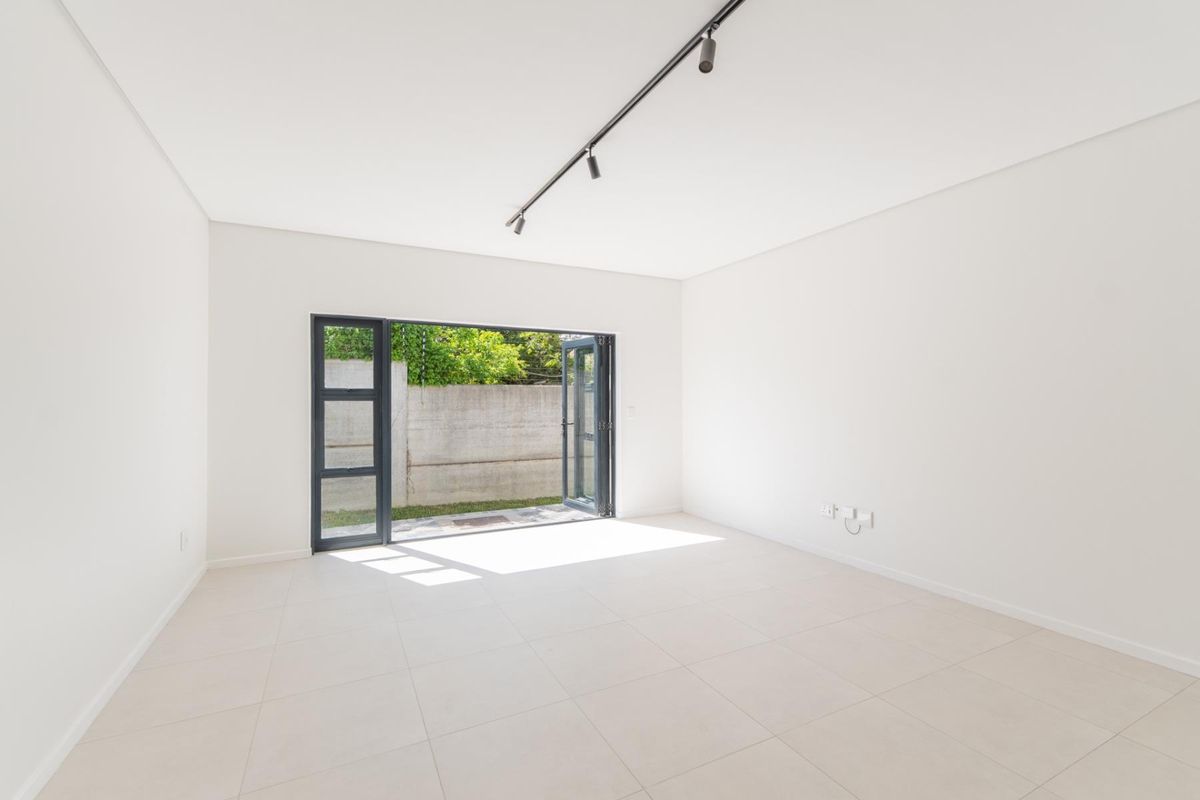 A bright, empty living room featuring neutral floor tiles, track lighting, and large folding doors that open directly to the rear garden area.