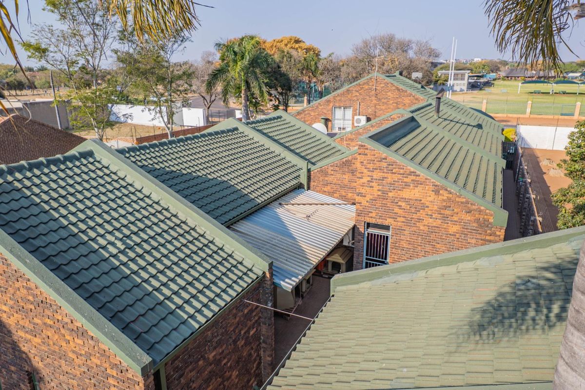 An elevated aerial view of the property showing the multi-pitched green tiled roof structure, brick facade, and a covered patio area.