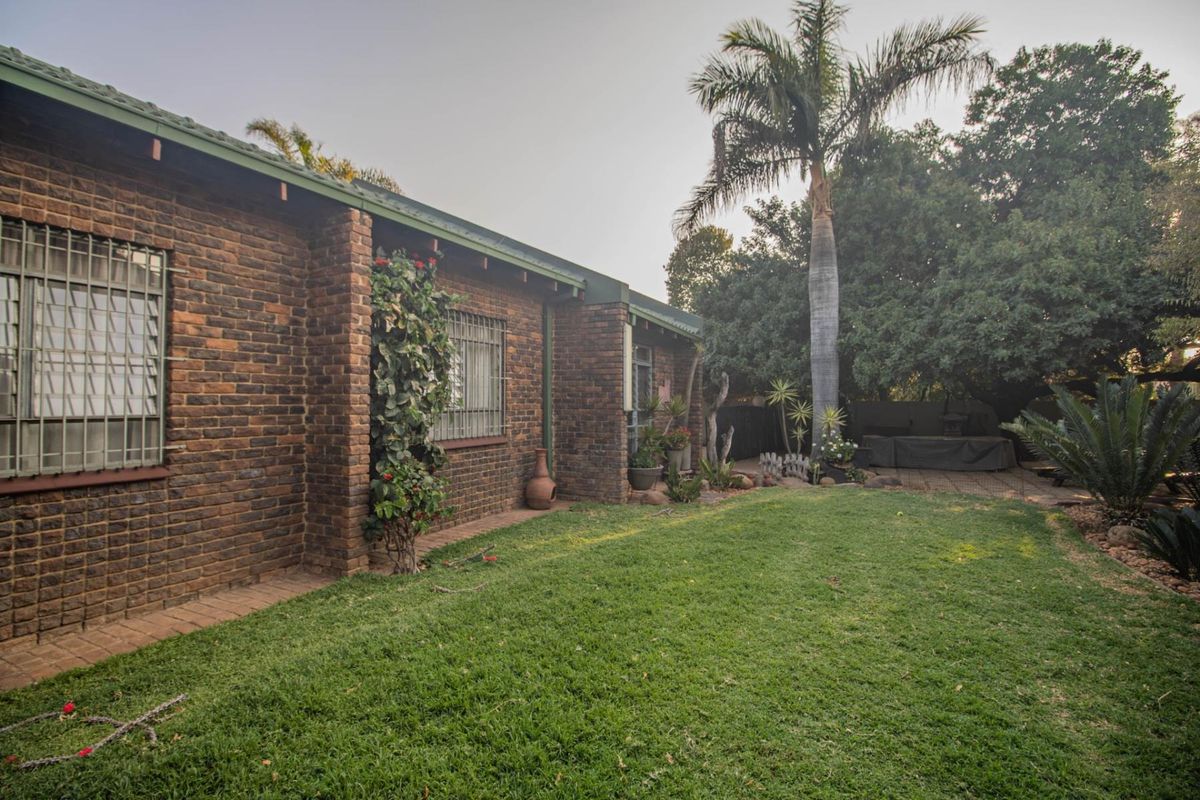 A view of the rear exterior of the house featuring a brick facade, security bars on windows, and a well-maintained lawn and garden area.