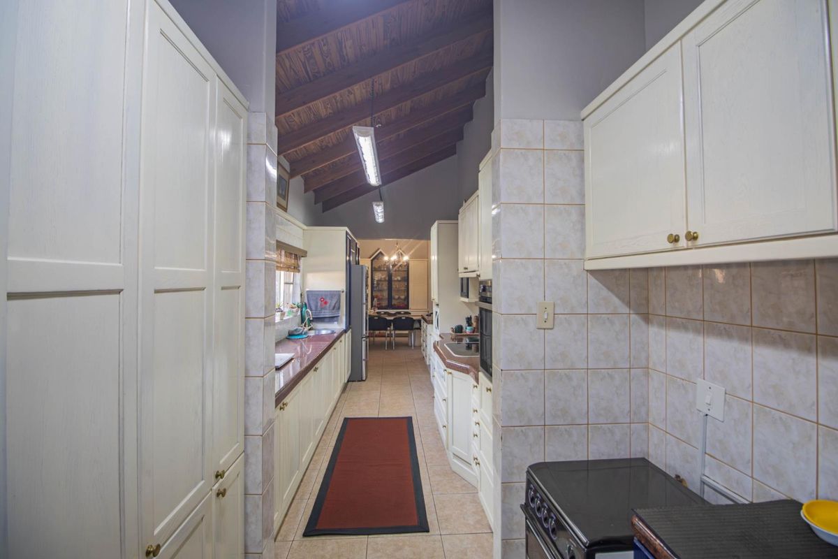 A galley-style kitchen featuring built-in cabinetry, tiled countertops, and a vaulted timber ceiling, leading into an adjacent dining area.