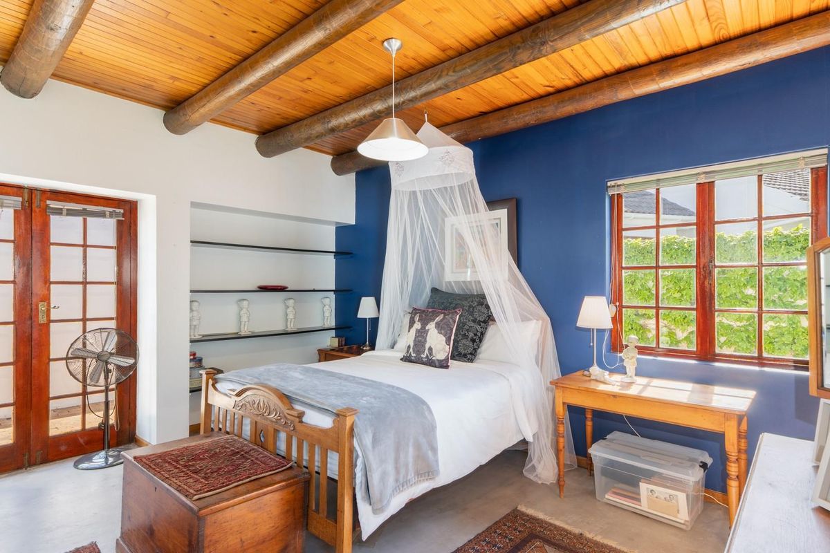 A bedroom featuring a rustic timber beam ceiling, polished concrete flooring, built-in shelving, and a large window with wooden frames.
