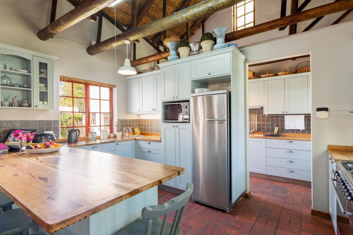 A charming kitchen featuring light blue cabinetry, wooden countertops, a central island, and a rustic exposed thatch roof with timber beams.
