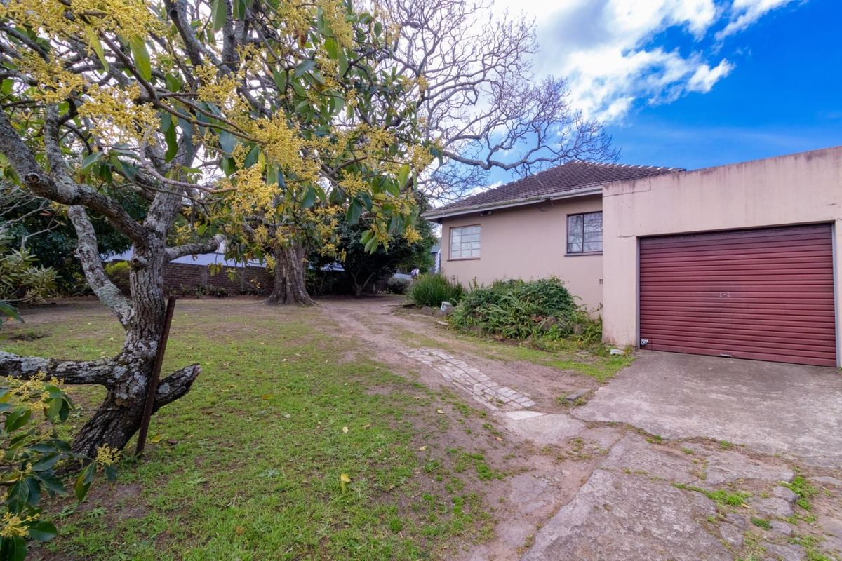 Exterior view of the property featuring a garage, concrete driveway, and a large garden area with mature trees.