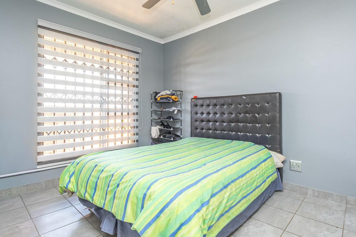 A bedroom featuring tiled flooring, a ceiling fan, and a window fitted with a modern zebra blind.