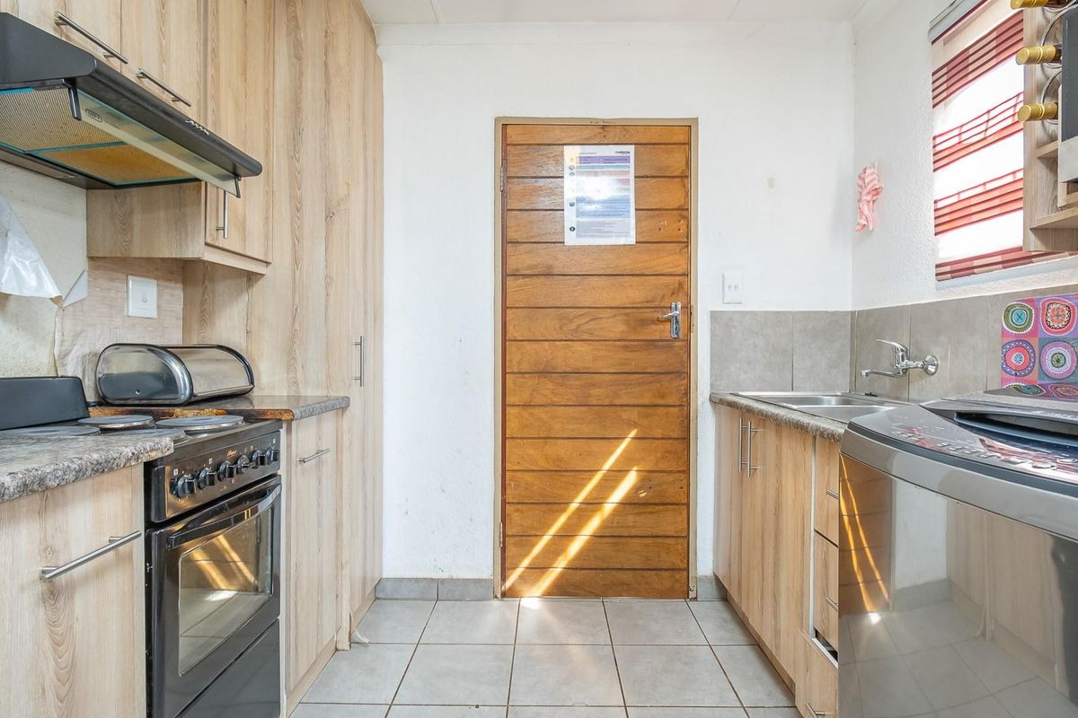 A functional kitchen featuring light wood-look cabinetry, granite-style countertops, a built-in oven with extractor fan, and a stainless steel sink.
