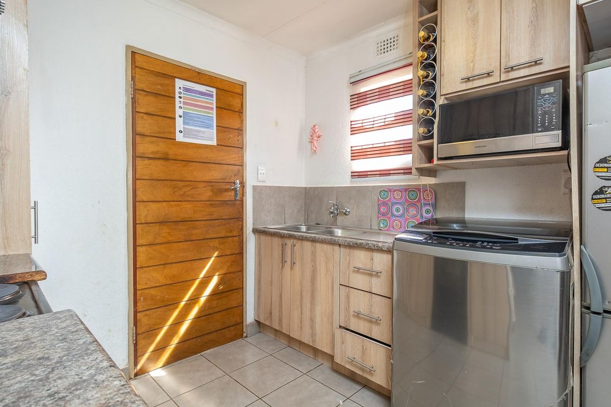 Compact kitchen area featuring light wood-look cabinetry, integrated microwave, stainless steel sink, and tiled flooring.