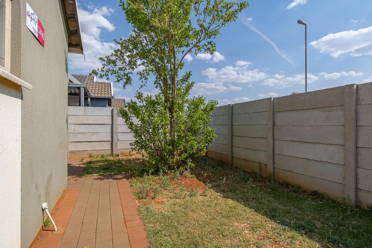A private rear garden area featuring a paved walkway, perimeter precast concrete walling, and established greenery.