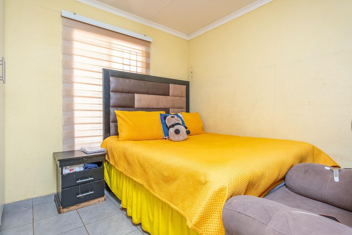 A functional bedroom featuring tiled flooring, built-in wardrobe storage, and a window with fitted blinds.