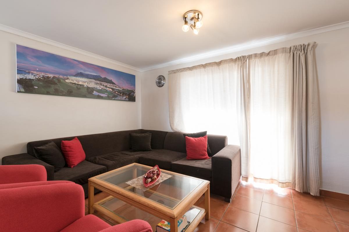 A comfortable living room featuring tiled flooring, neutral walls, and large windows with curtains, providing a bright and functional space.
