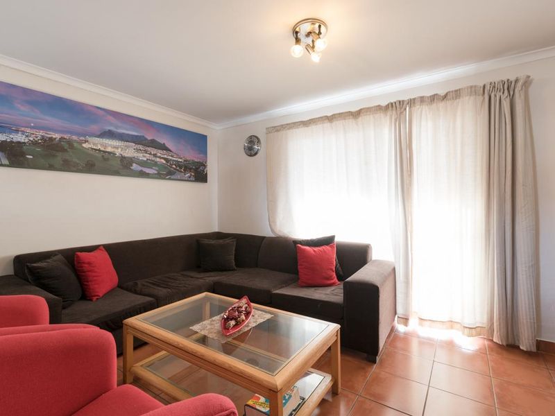 A comfortable living room featuring tiled flooring, neutral walls, and large windows with curtains, providing a bright and functional space.