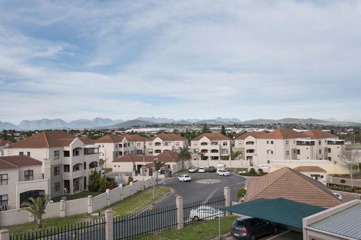 An elevated aerial view of the apartment complex, showcasing the residential buildings, paved access roads, and surrounding mountain landscape.
