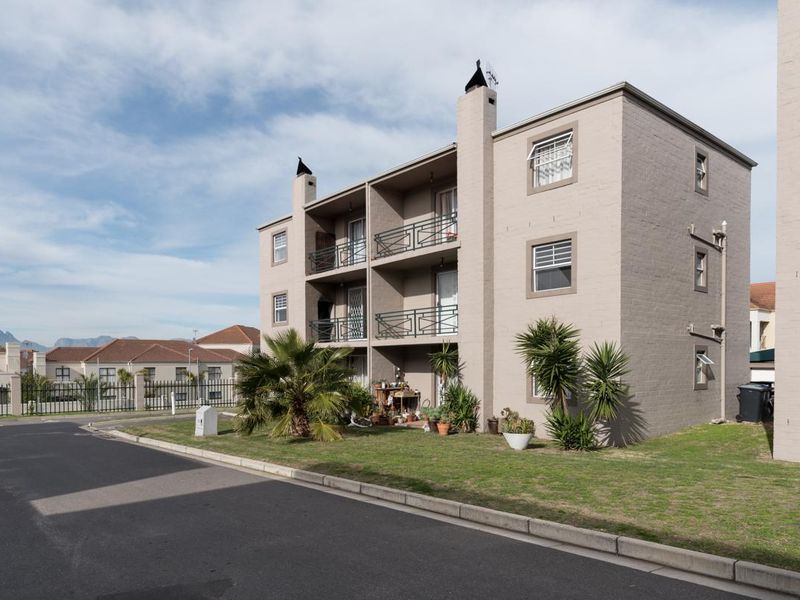 Exterior view of a three-story apartment building featuring balconies with metal railings, brick facade, and surrounding landscaped grounds.