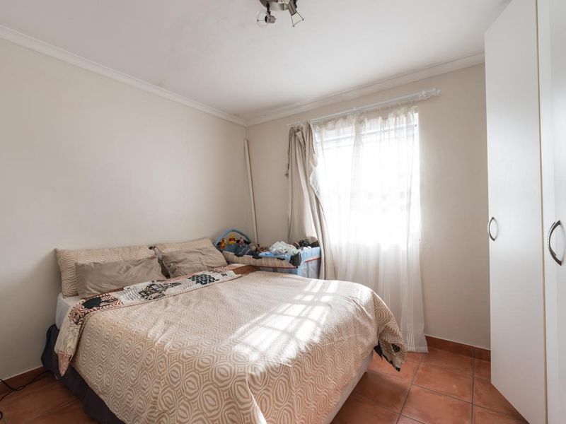 A functional bedroom featuring tiled flooring, a built-in wardrobe, and natural light from the window.
