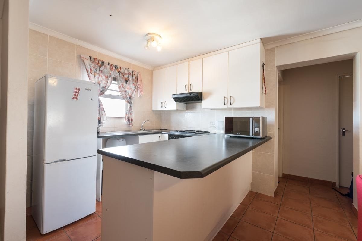 A functional kitchen featuring white cabinetry, a dark laminate breakfast bar, tiled backsplash, and tiled flooring, providing a practical layout for daily use.