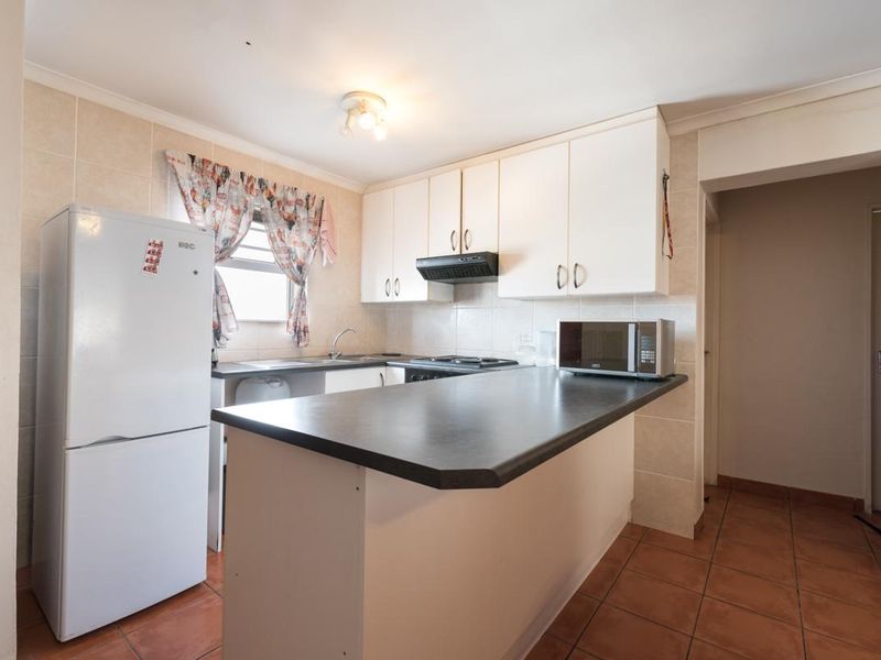A functional kitchen featuring white cabinetry, a dark laminate breakfast bar, tiled backsplash, and tiled flooring, providing a practical layout for daily use.
