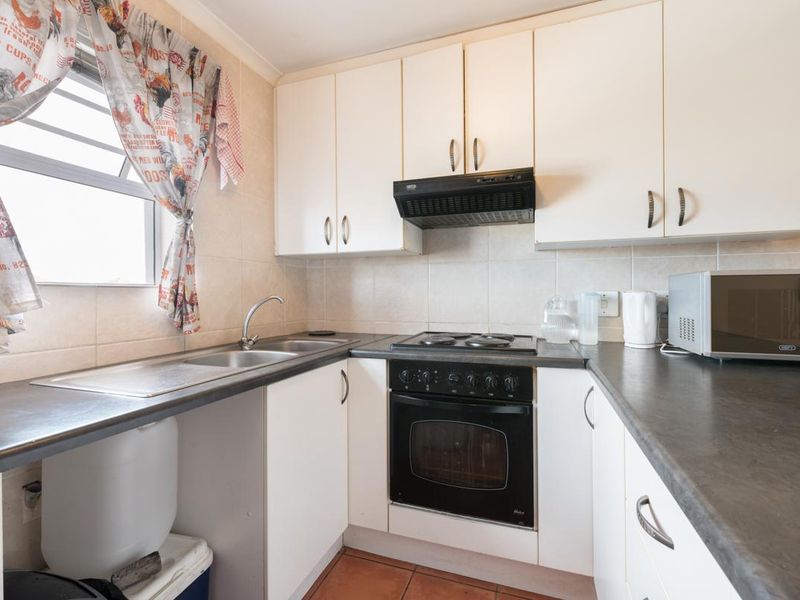 Compact kitchen featuring white built-in cabinetry, dark laminate countertops, tiled backsplash, and integrated oven with electric hob.