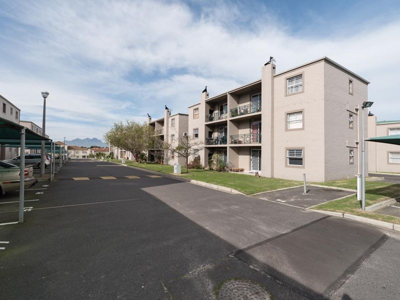 Exterior view of a multi-story apartment complex featuring brick facades, private balconies, and designated covered parking bays within a paved residential estate.