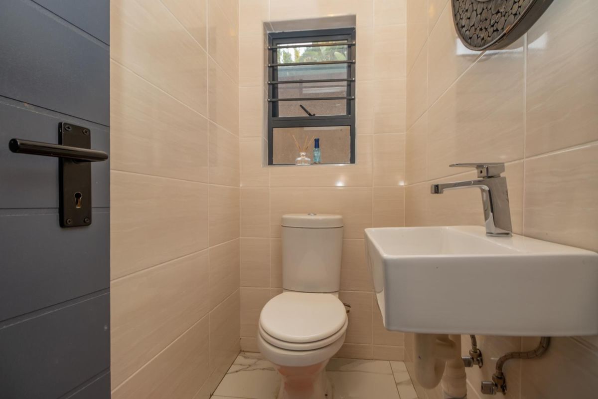 A compact guest bathroom featuring modern wall tiling, a wall-mounted basin, and a low-profile toilet with a security-barred window.
