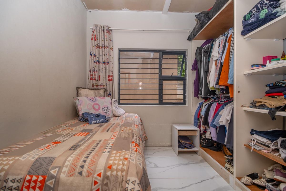 A compact bedroom featuring a built-in wardrobe, tiled flooring, and a window with security bars.