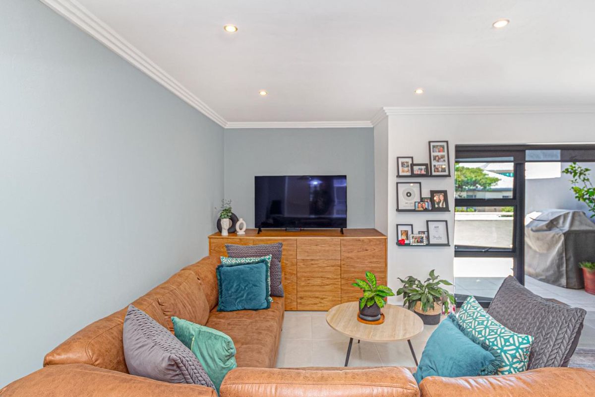 A well-maintained living room featuring tiled flooring, recessed downlighting, and a large glass door providing access to an outdoor area.