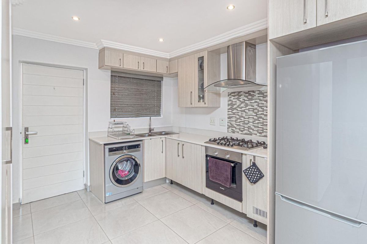 Modern kitchen featuring light wood cabinetry, gas hob, built-in oven, extractor fan, mosaic backsplash, and tiled flooring with integrated laundry space.