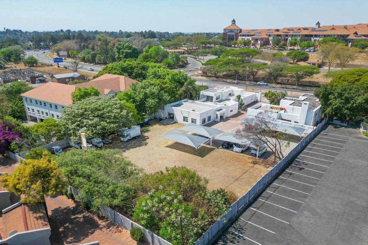 Aerial view of a commercial property featuring a large paved parking area, shade sail structures, and multiple white building blocks.