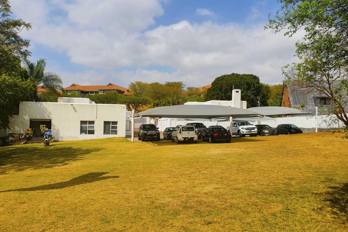 Exterior view of a commercial property featuring a large lawn area and covered parking bays for multiple vehicles.